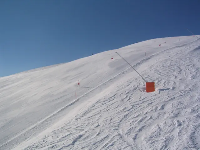 Ski tracks cross a sunlit slope beside an orange piste marker.