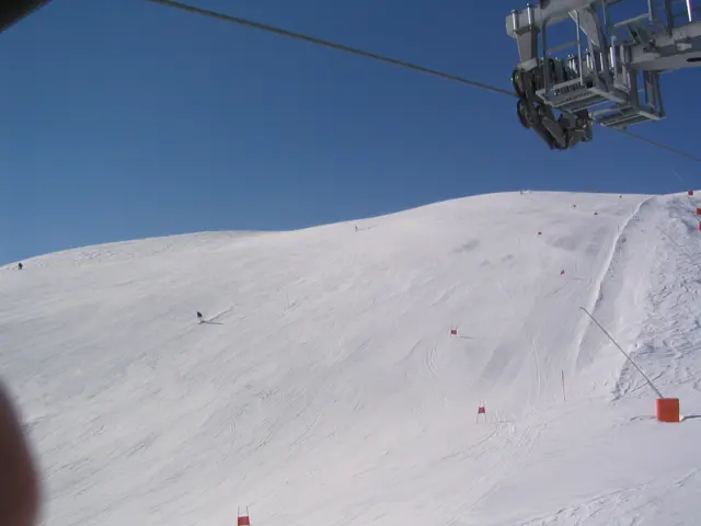 A chairlift passes overhead above a broad white slope and marker pole.