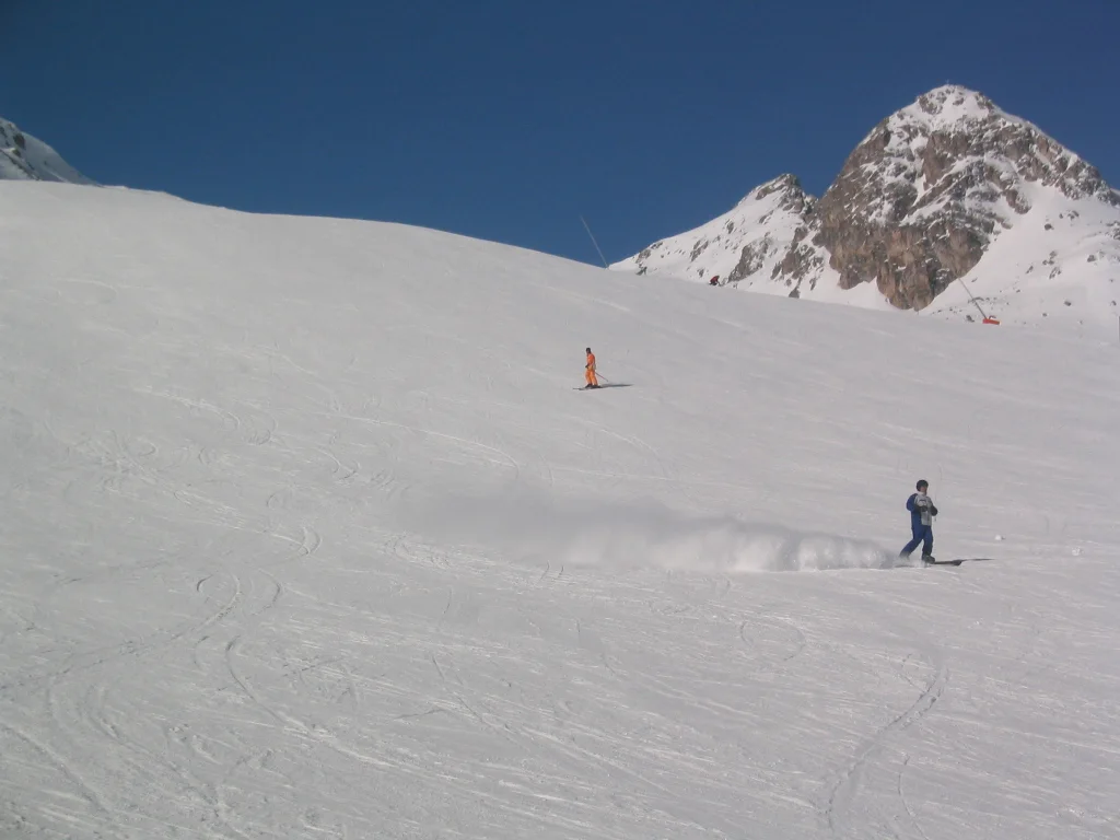 Small skiers descend an open slope beneath a pointed rocky peak.