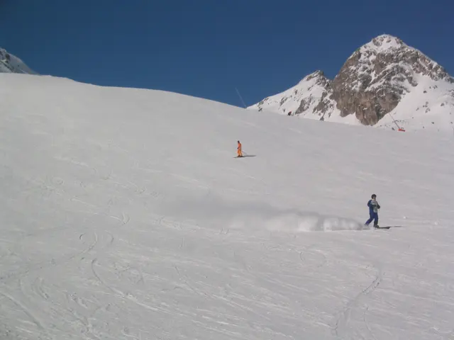 Small skiers descend an open slope beneath a pointed rocky peak.