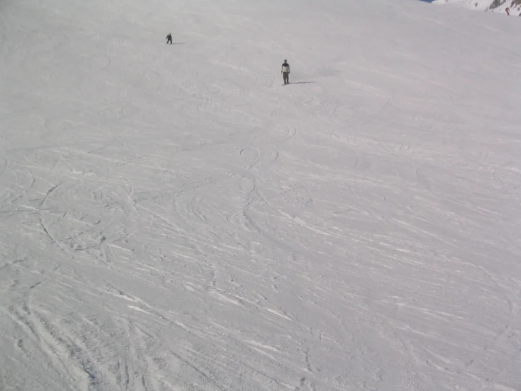 Fine ski tracks curve across a pale slope beneath distant figures.