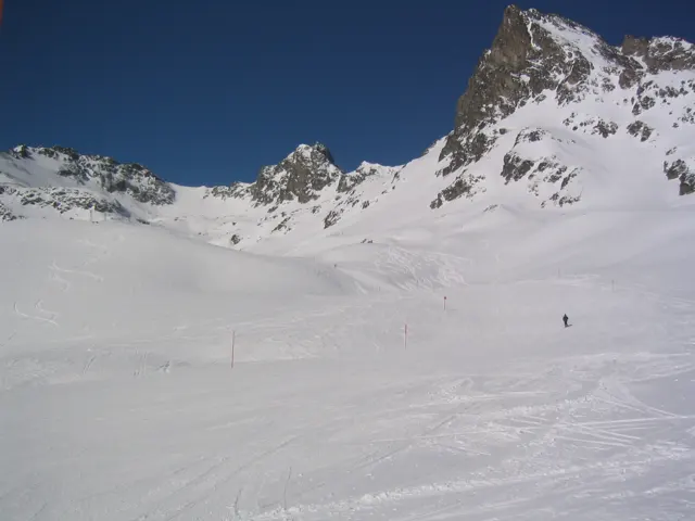 A wide snow basin opens beneath jagged rocky peaks and deep blue sky.