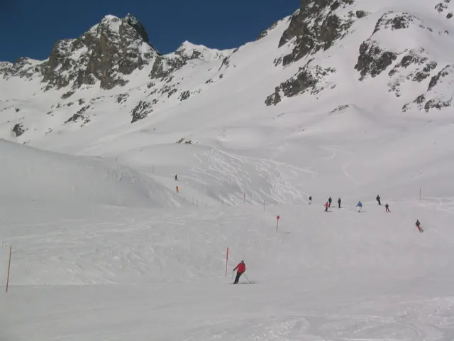 Small skiers form a loose line across a wide slope beneath rocky peaks.