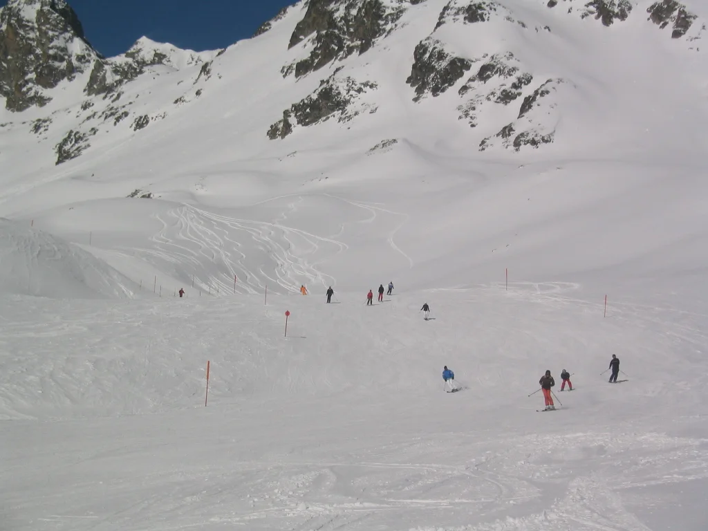 Several skiers descend a broad snow bowl surrounded by steep mountain faces.