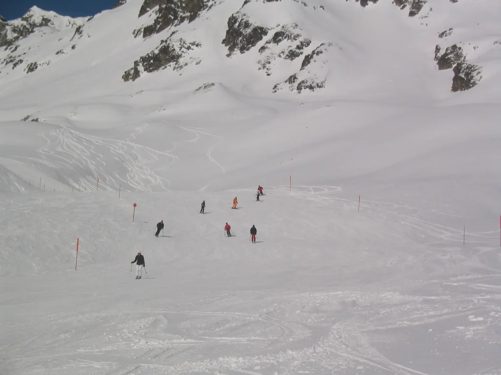 Scattered figures move across the snow below rocky ridges and shallow gullies.