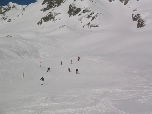 Scattered figures move across the snow below rocky ridges and shallow gullies.