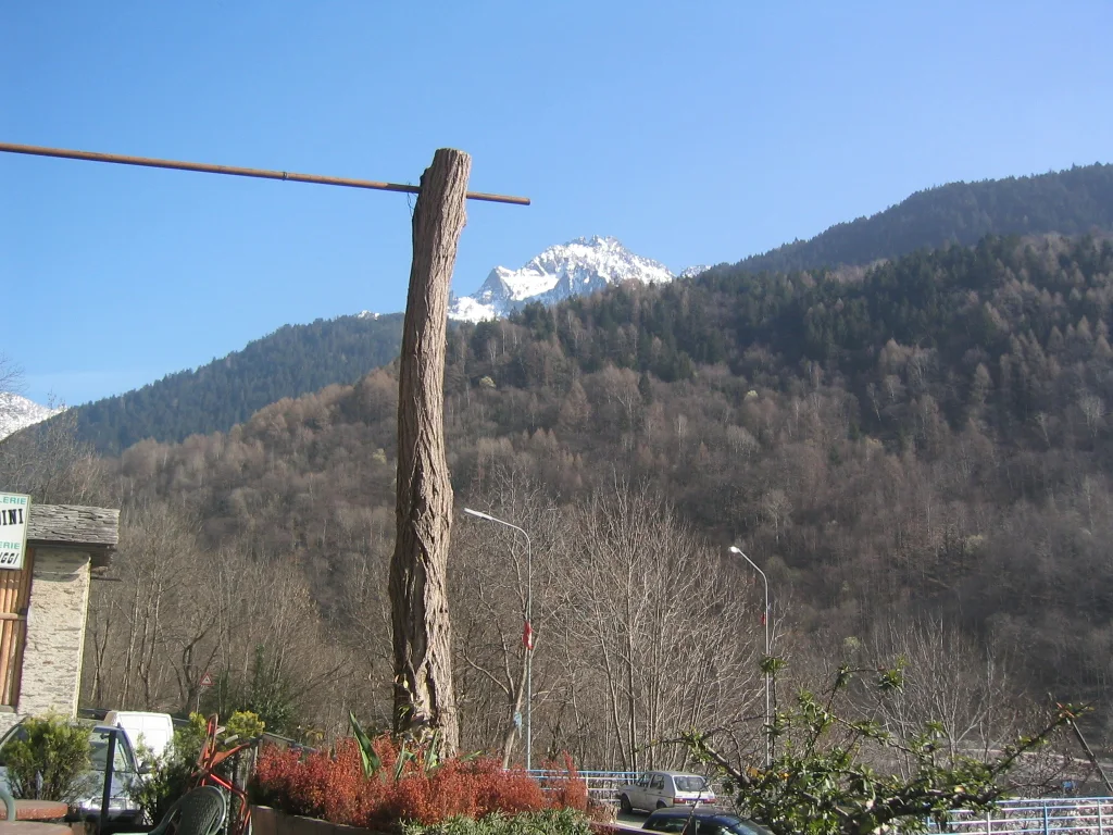 A terrace post and flower boxes frame a wooded mountainside and distant snow peak.