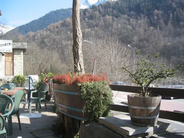 Wooden barrel planters and outdoor chairs stand on a terrace facing the mountains.