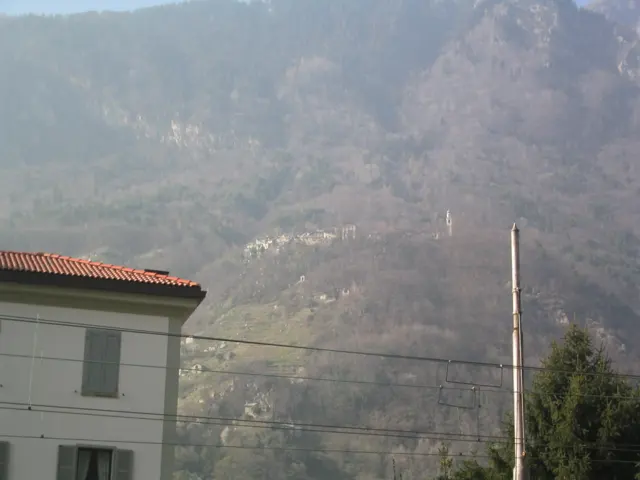 A pale building and roof edge sit beneath a hazy wooded mountain slope.