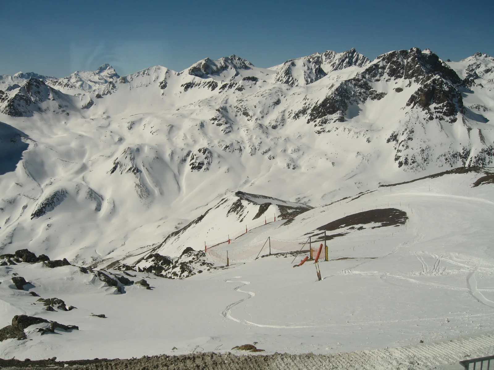 Ski tracks and lift structures cross a broad snowy basin below jagged peaks.