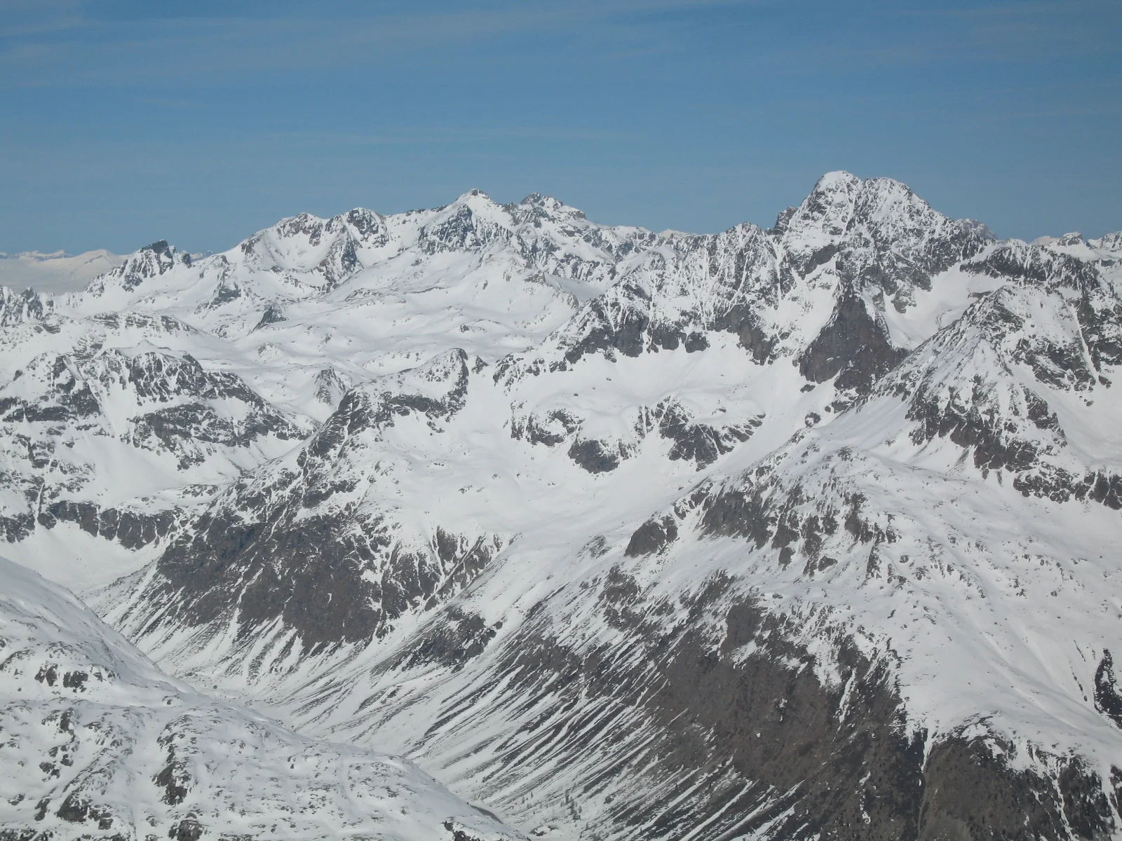 Successive jagged peaks and snow-filled gullies stretch across a wide mountain panorama.