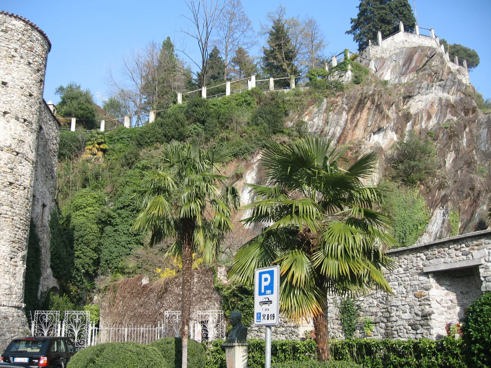 Palm trees grow beside a round stone tower and a rocky planted slope.