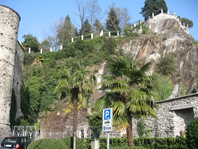 Palm trees grow beside a round stone tower and a rocky planted slope.