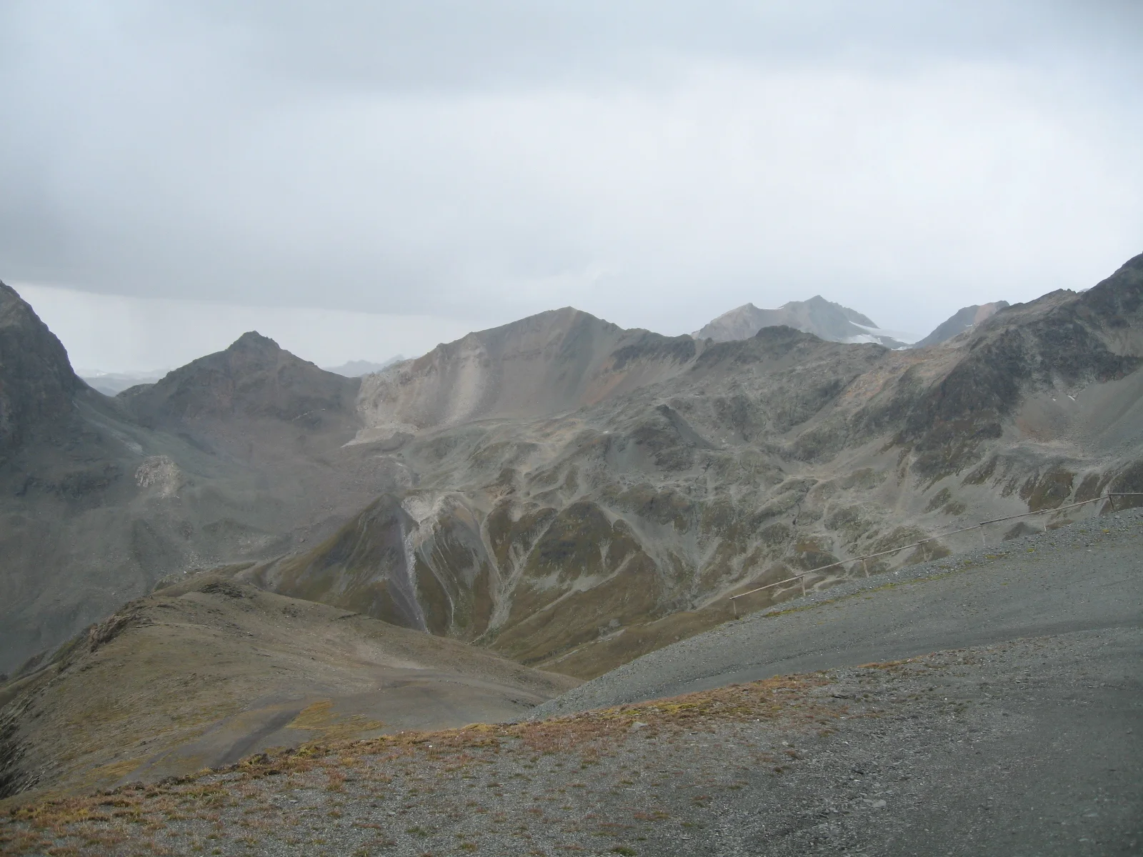 A rocky, largely bare mountain basin lies beneath a low gray sky.