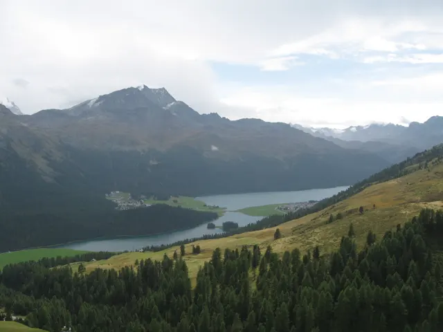 A pale lake curves between forested slopes below a dark mountain ridge.