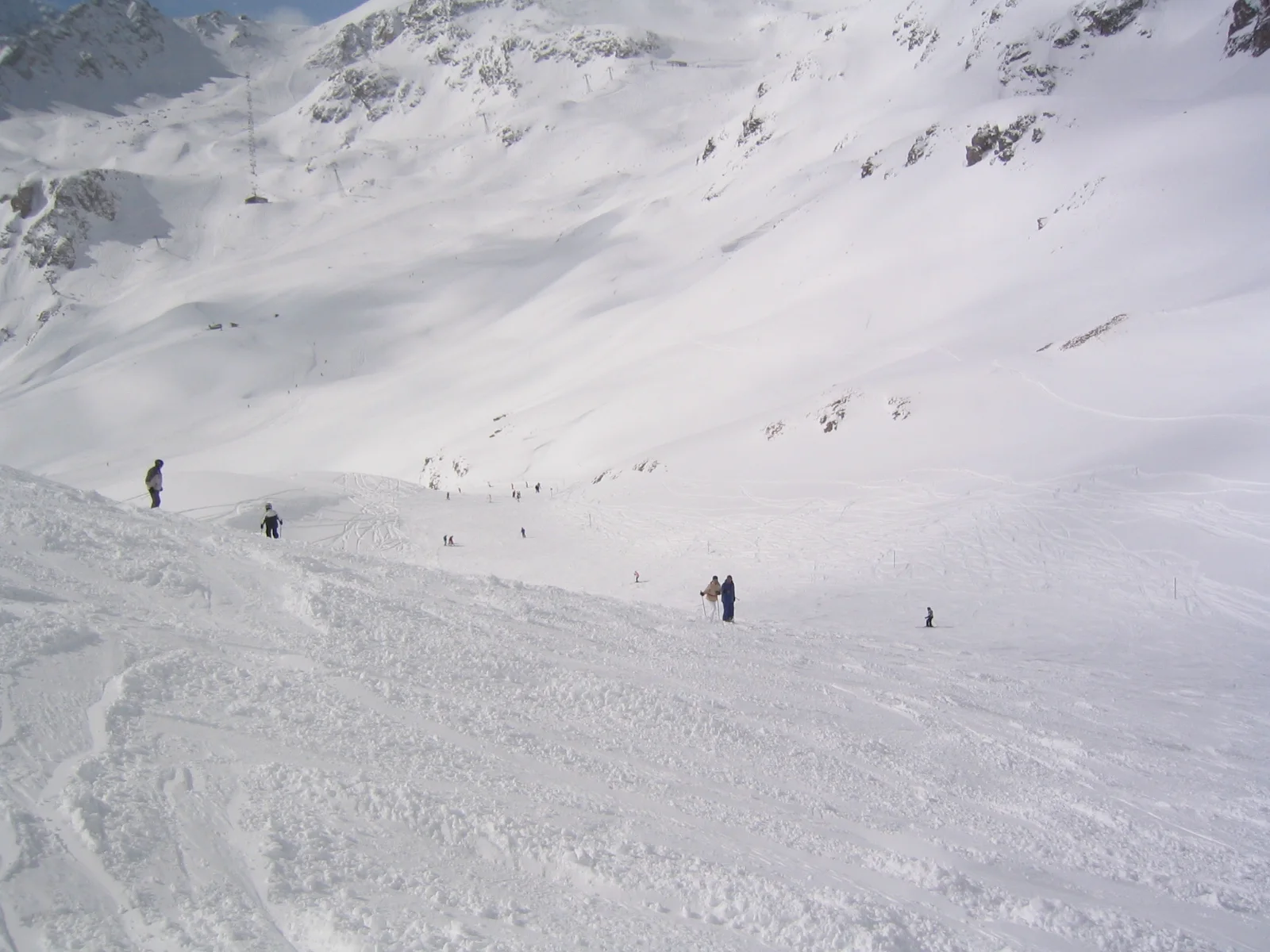 Small skiers move through a snowy hollow beneath steep white slopes.