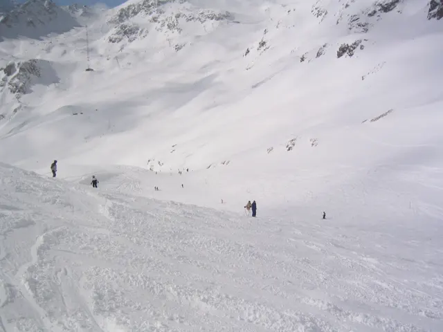 Small skiers move through a snowy hollow beneath steep white slopes.