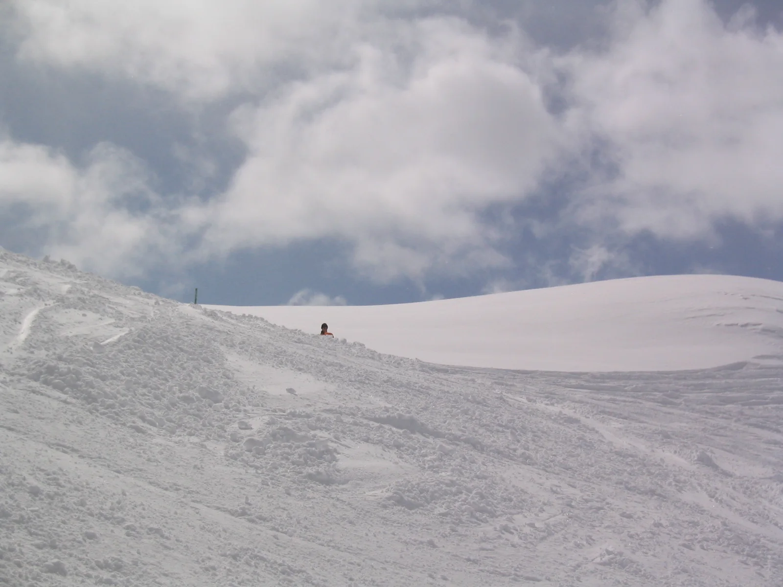 A tracked snow slope rises toward a smooth crest beneath thick white clouds.