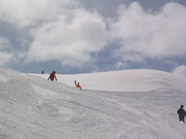 Several small figures stand near a snowy crest beneath a cloud-filled sky.