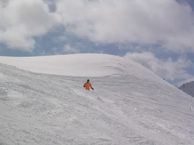 A figure in orange crosses tracked snow below a smooth white ridge.