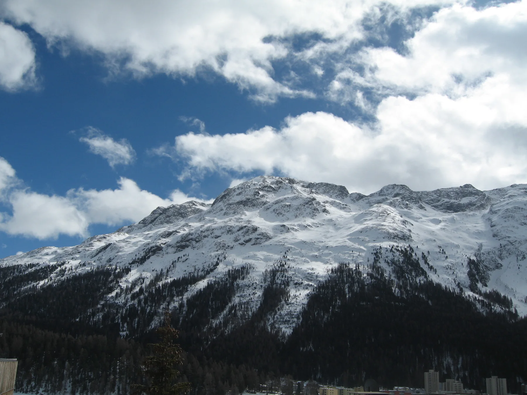 Sunlight catches snowy mountain slopes below patches of blue sky and white clouds.