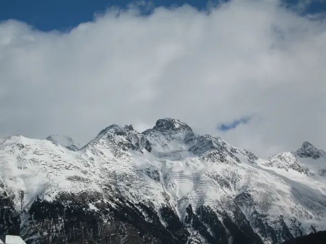 A rugged mountain crown emerges above snowy slopes beneath drifting clouds.