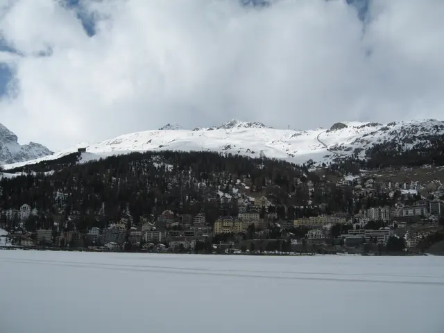 A broad frozen lake lies below wooded slopes and a snow-covered ridge.