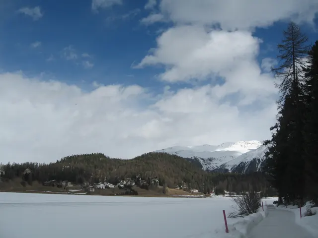 A snowy shore lined with trees follows the edge of a frozen lake toward distant hills.