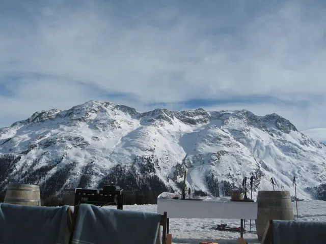 Outdoor seats face a broad snowy mountain ridge beyond a terrace.
