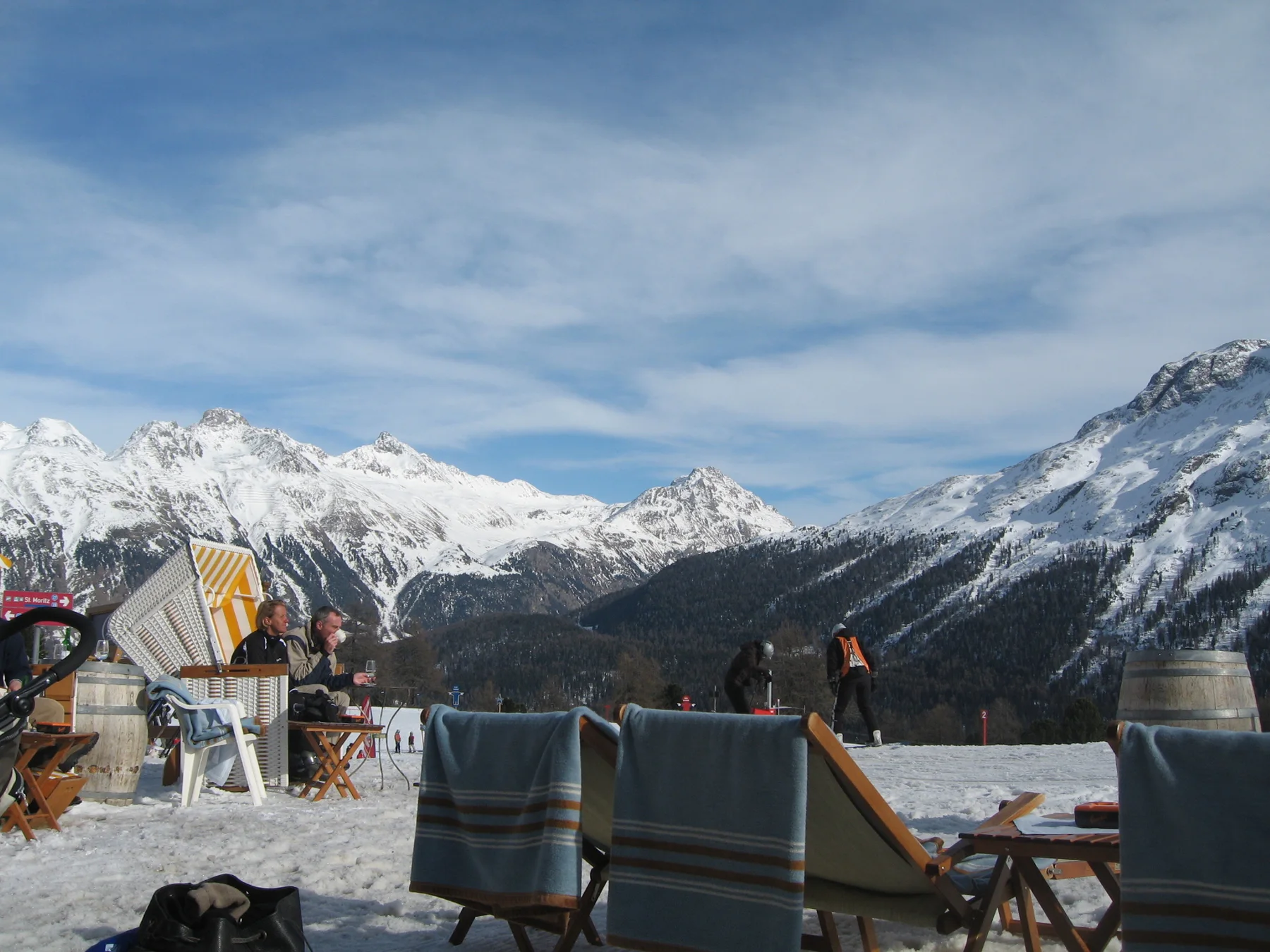 Chairs, tables and terrace structures stand before a wide range of snow-covered mountains.