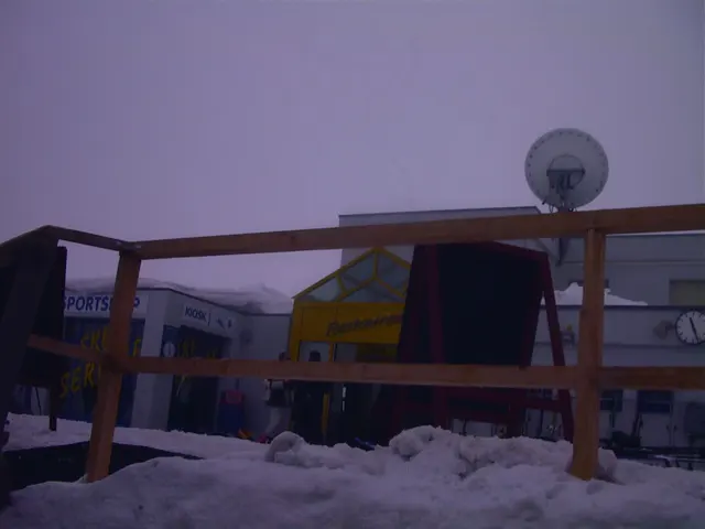 A wooden railing and terrace furnishings sit in snow beneath a pale, misty sky.