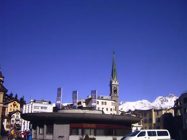 A slender church spire rises above town buildings against a deep blue sky.