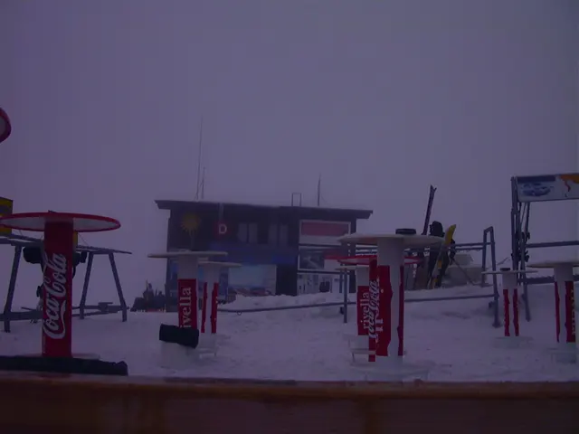 Ski equipment, signs and a low building occupy a snowy lift area in muted light.