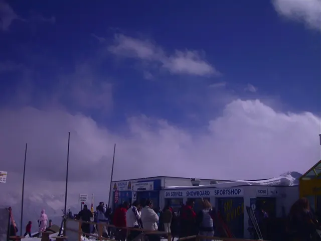 People gather near a mountain building beneath a blue opening in heavy clouds.