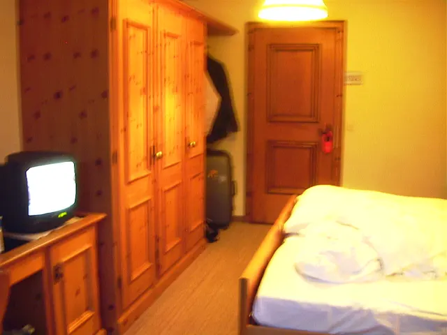 Warm light fills a room with wooden cupboards, a bed and a small television.