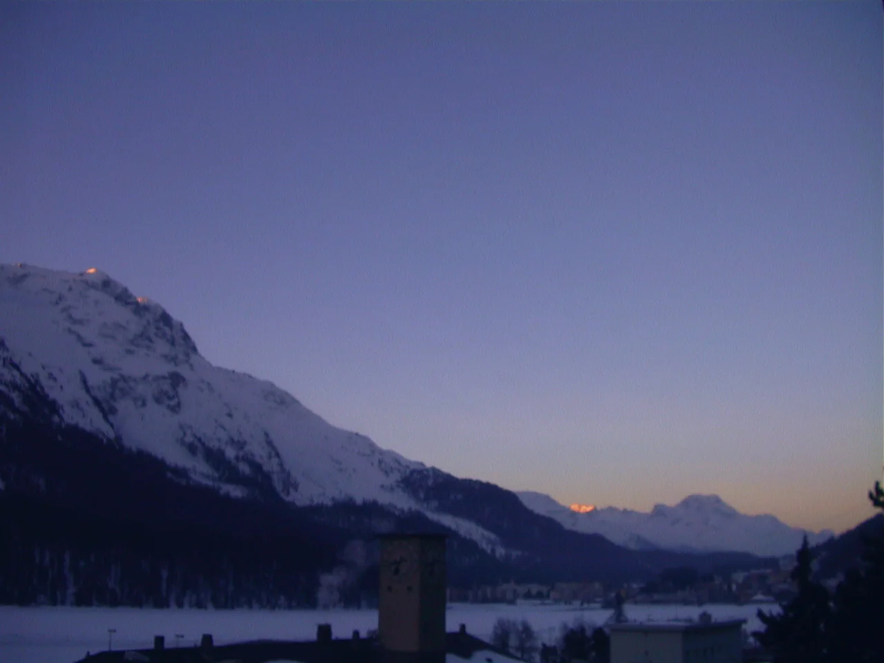 A snowy valley opens between dark mountains beneath a faint warm band at the horizon.