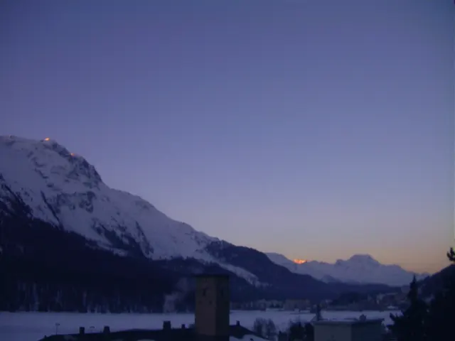 A snowy valley opens between dark mountains beneath a faint warm band at the horizon.