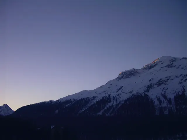 A snowy mountain slope falls into shadow beneath a pale twilight sky.