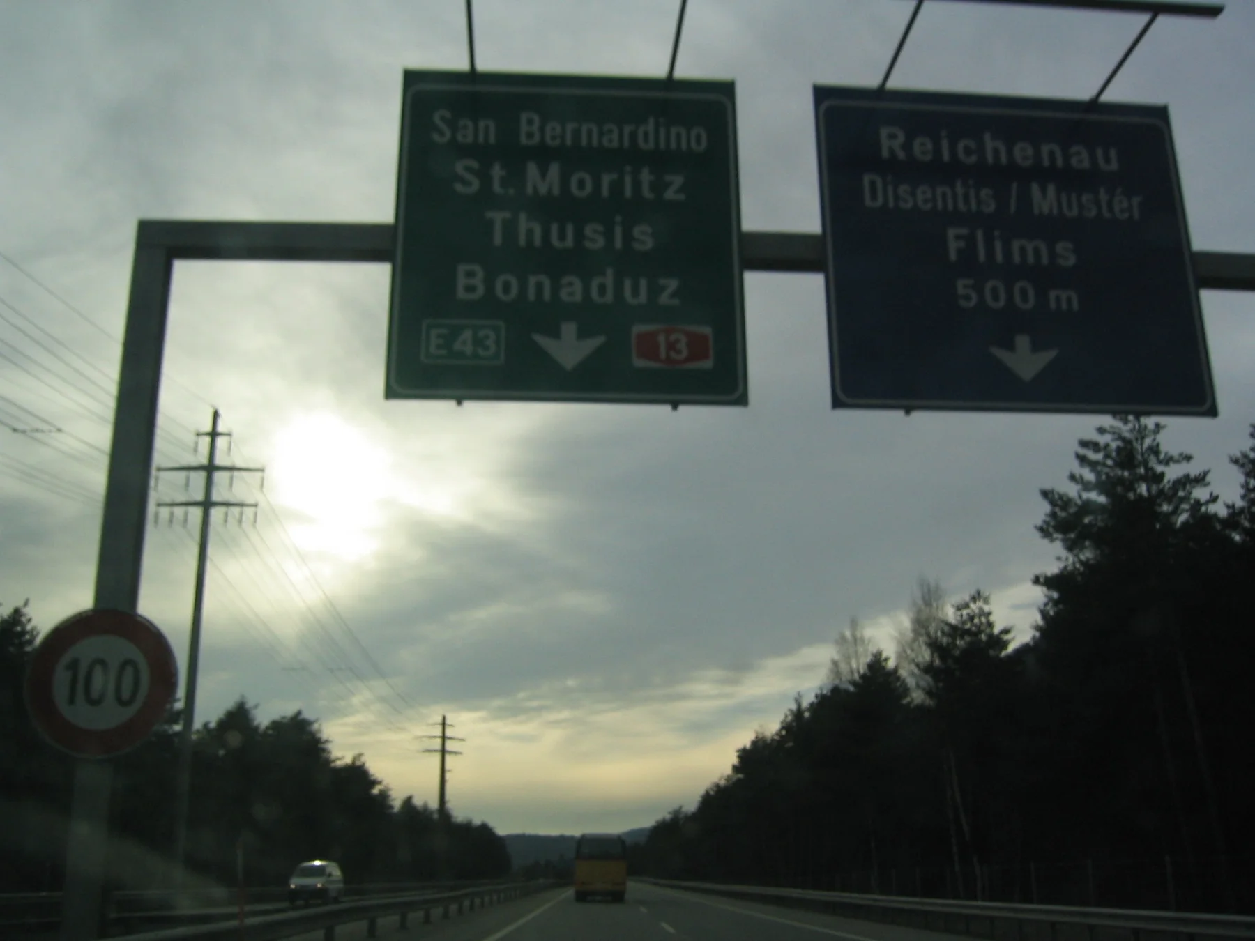 Overhead road signs silhouette against a low sun and clouded sky.