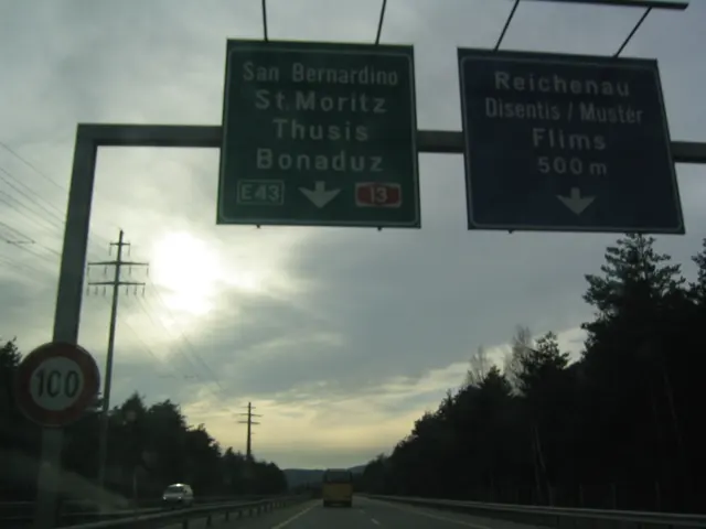 Overhead road signs silhouette against a low sun and clouded sky.