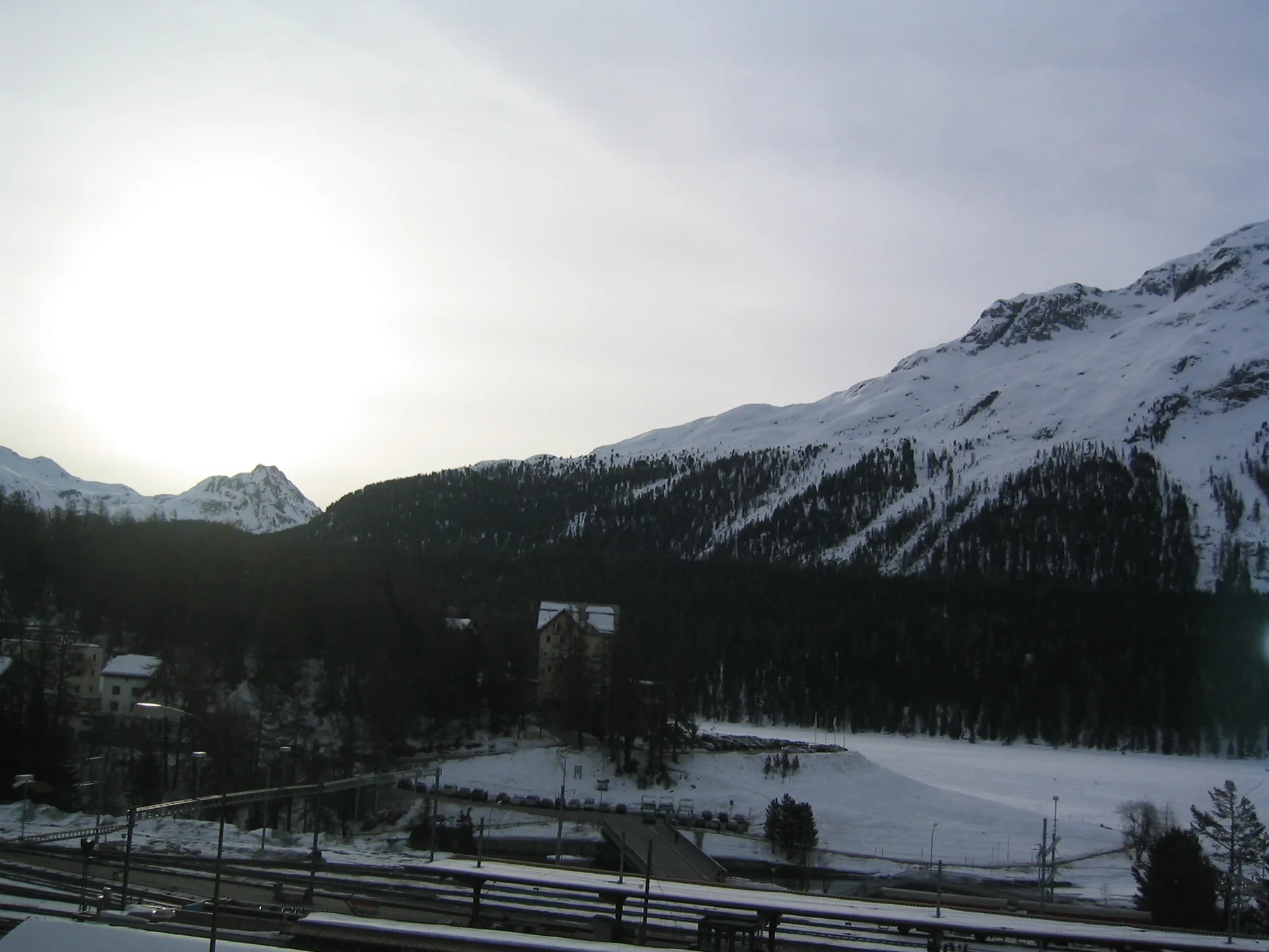A bright opening in the sky lights a snowy valley beneath dark mountain slopes.