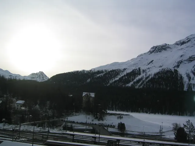 A bright opening in the sky lights a snowy valley beneath dark mountain slopes.