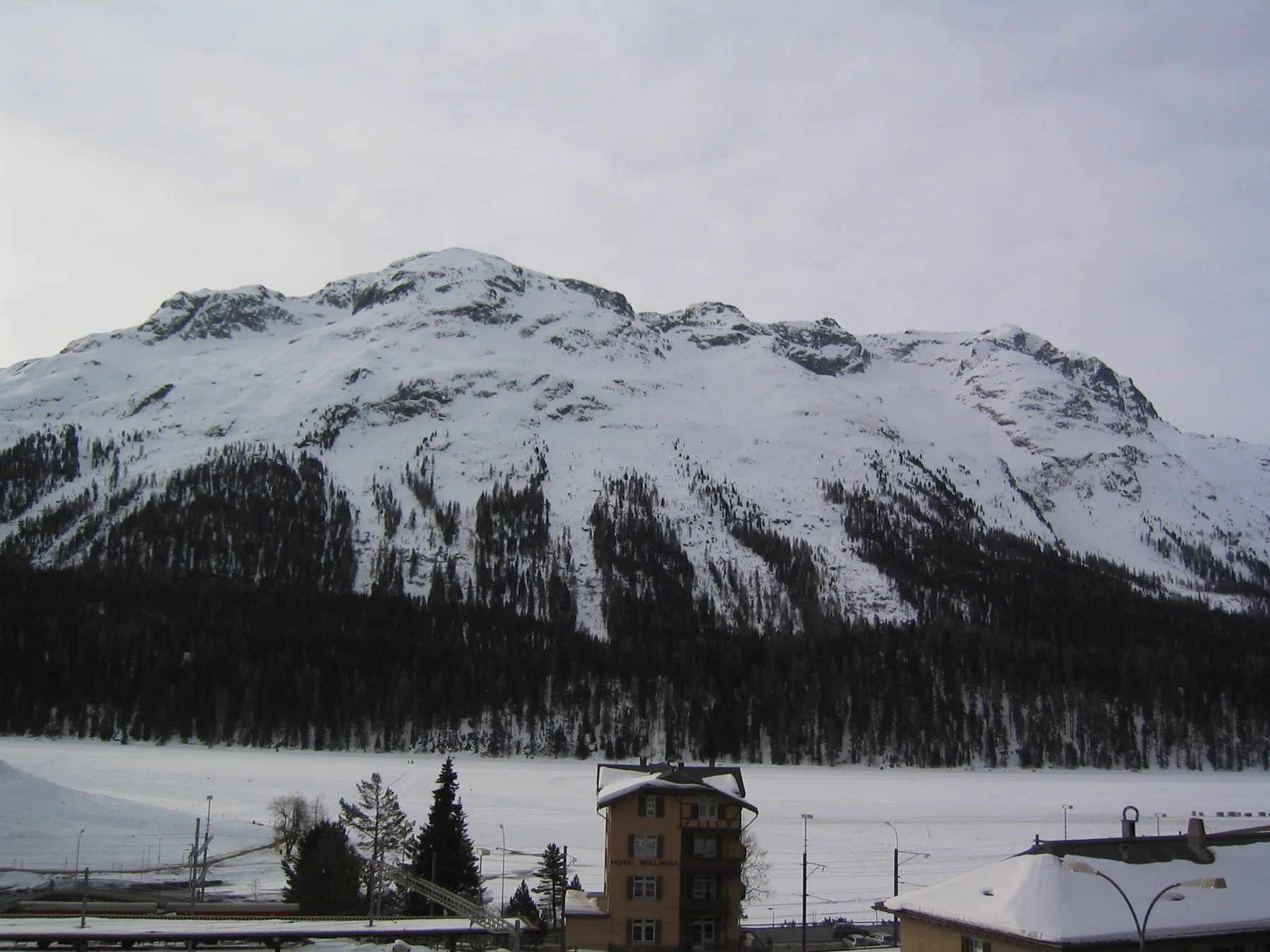 A broad snowy ridge rises beyond a small tower and snow-covered roofs.