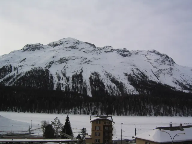 A broad snowy ridge rises beyond a small tower and snow-covered roofs.
