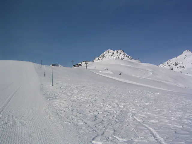 A marked snowy track leads toward a pointed white peak under blue sky.