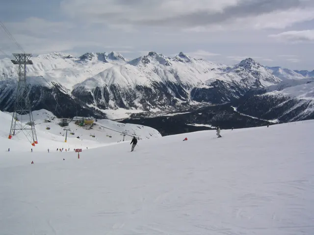 Scattered skiers cross a wide slope overlooking a deep mountain valley.