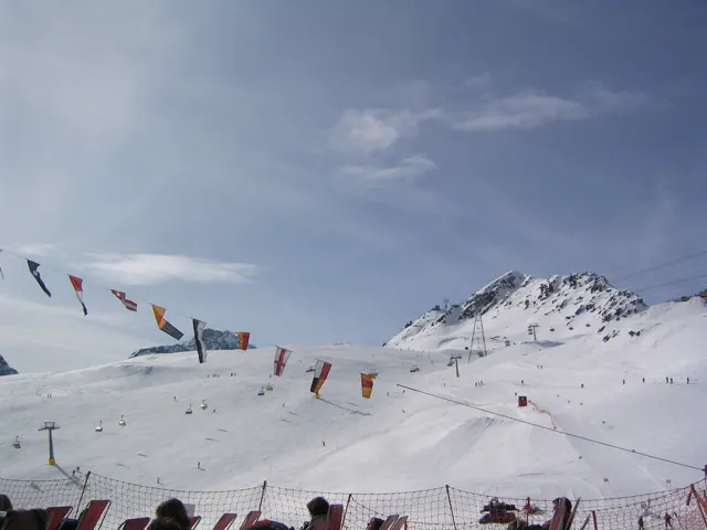 A line of small colorful flags stretches above a snowy mountain recreation area.