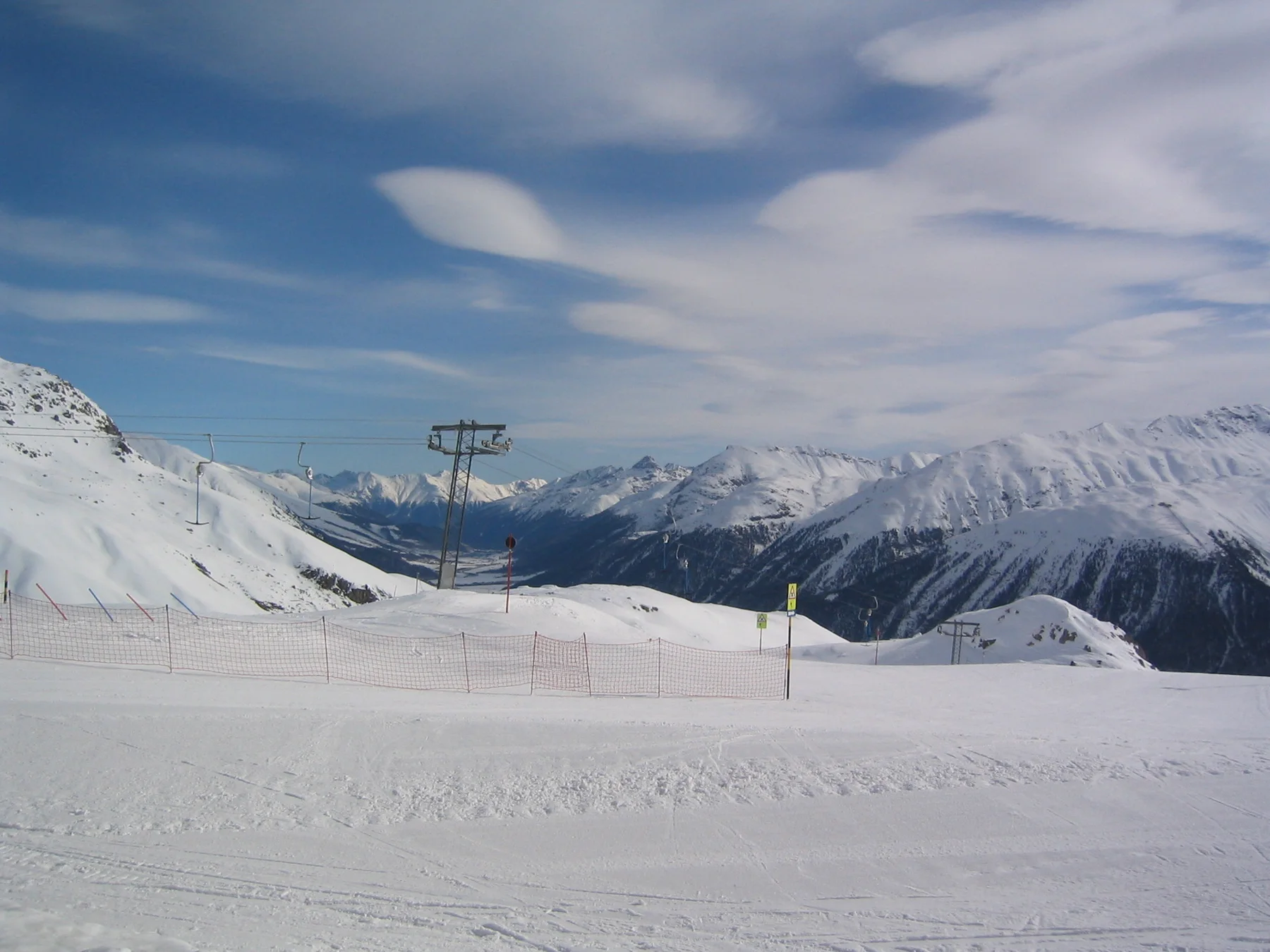 A broad ski slope opens toward mountains beneath thin, streaked clouds.