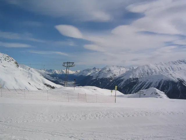 A broad ski slope opens toward mountains beneath thin, streaked clouds.