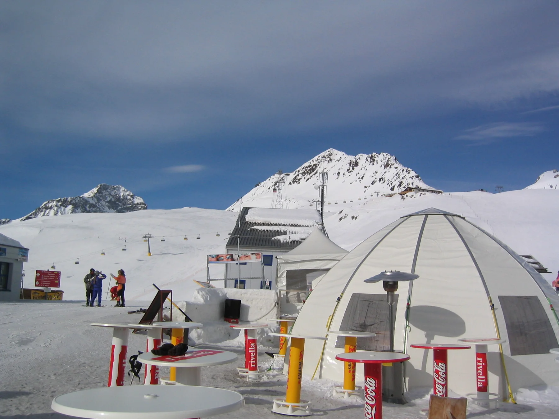 A dome-shaped terrace structure and bright table supports sit below a snowy summit.